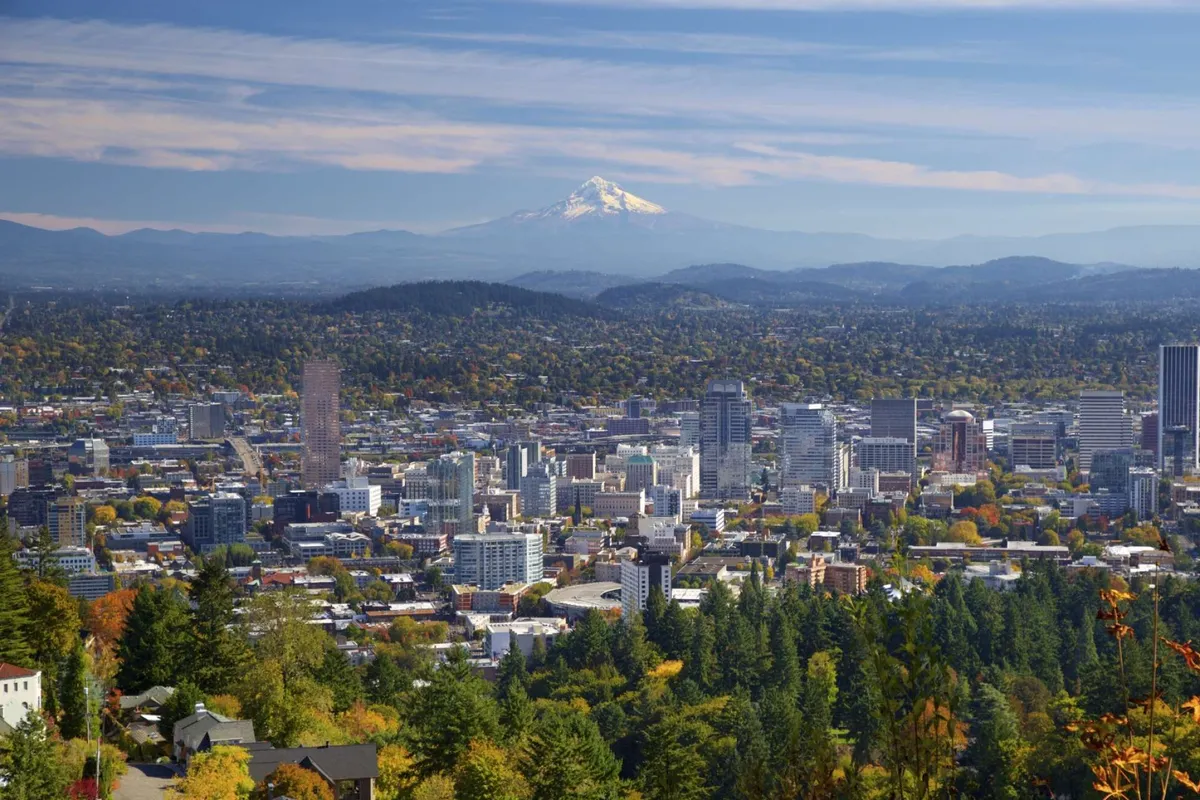 A sweeping view from the hills, featuring Mount Hood, the city skyline, and colorful fall foliage. The perspective highlights both natural beauty and urban vibrancy, suggesting opportunities for exploration and seasonal festivals.
