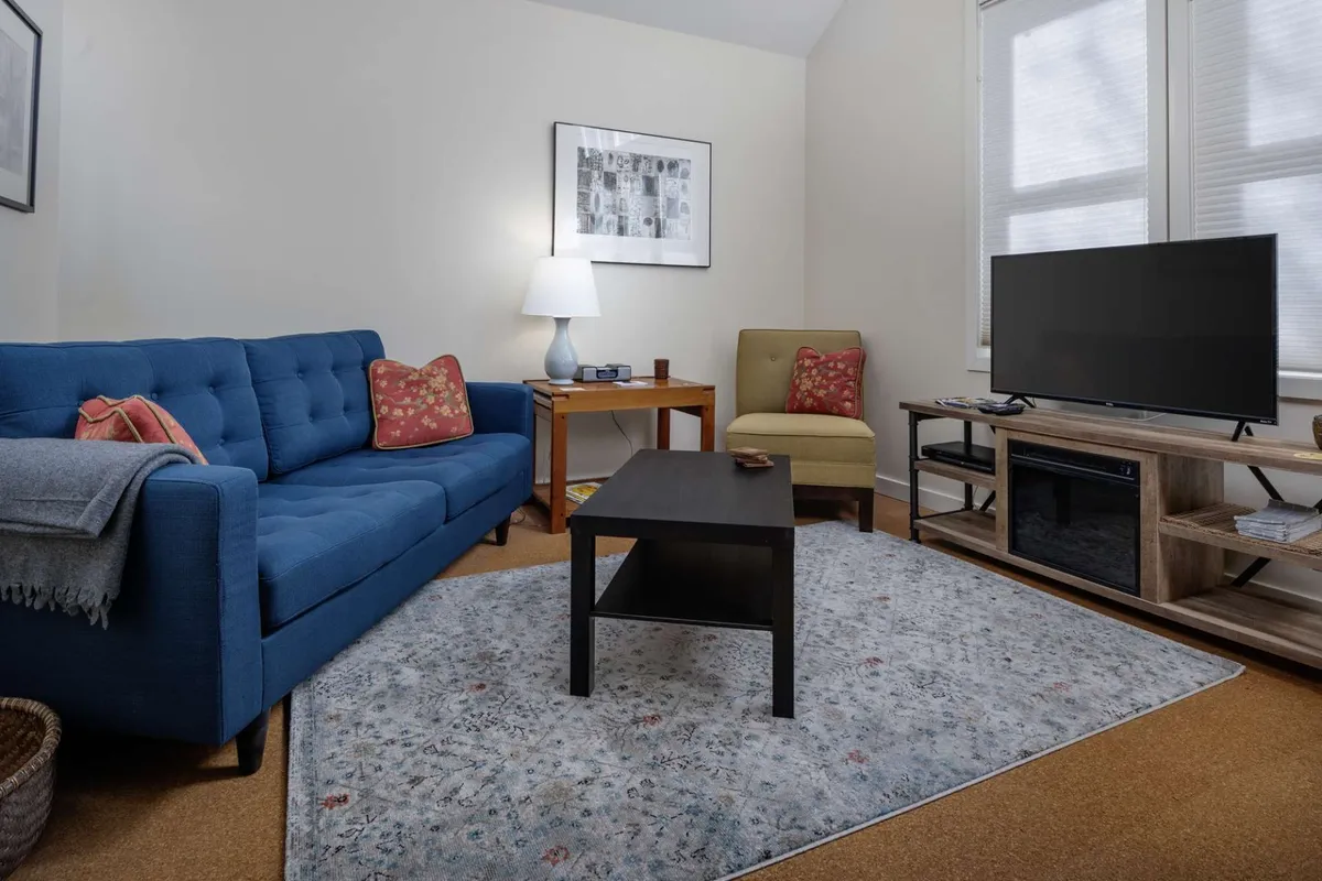 The image showcases a cozy, inviting living space featuring a plush blue sofa, an accent chair, a stylish coffee table, a television, and a warm lamp. The décor is welcoming and perfect for relaxation, reading, or sharing quiet moments together.
