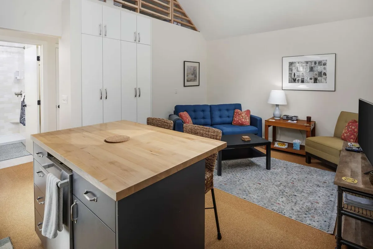 This image captures an inviting open-concept living and kitchen area. The space features a prominent blue sofa facing a large TV unit, with a wooden kitchen island and stylish artwork on the walls. The island offers functional seating, bridging the kitchen and living room for both cooking and socializing.