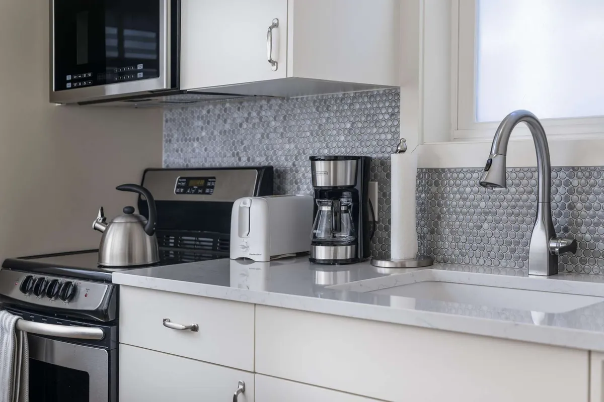 A functional, welcoming kitchen space featuring a sleek kettle, coffee maker, toaster, and ample counter space. The scene suggests convenience for morning routines or preparing meals, with a bright and organized aesthetic that hints at a space ready for productivity and relaxation.